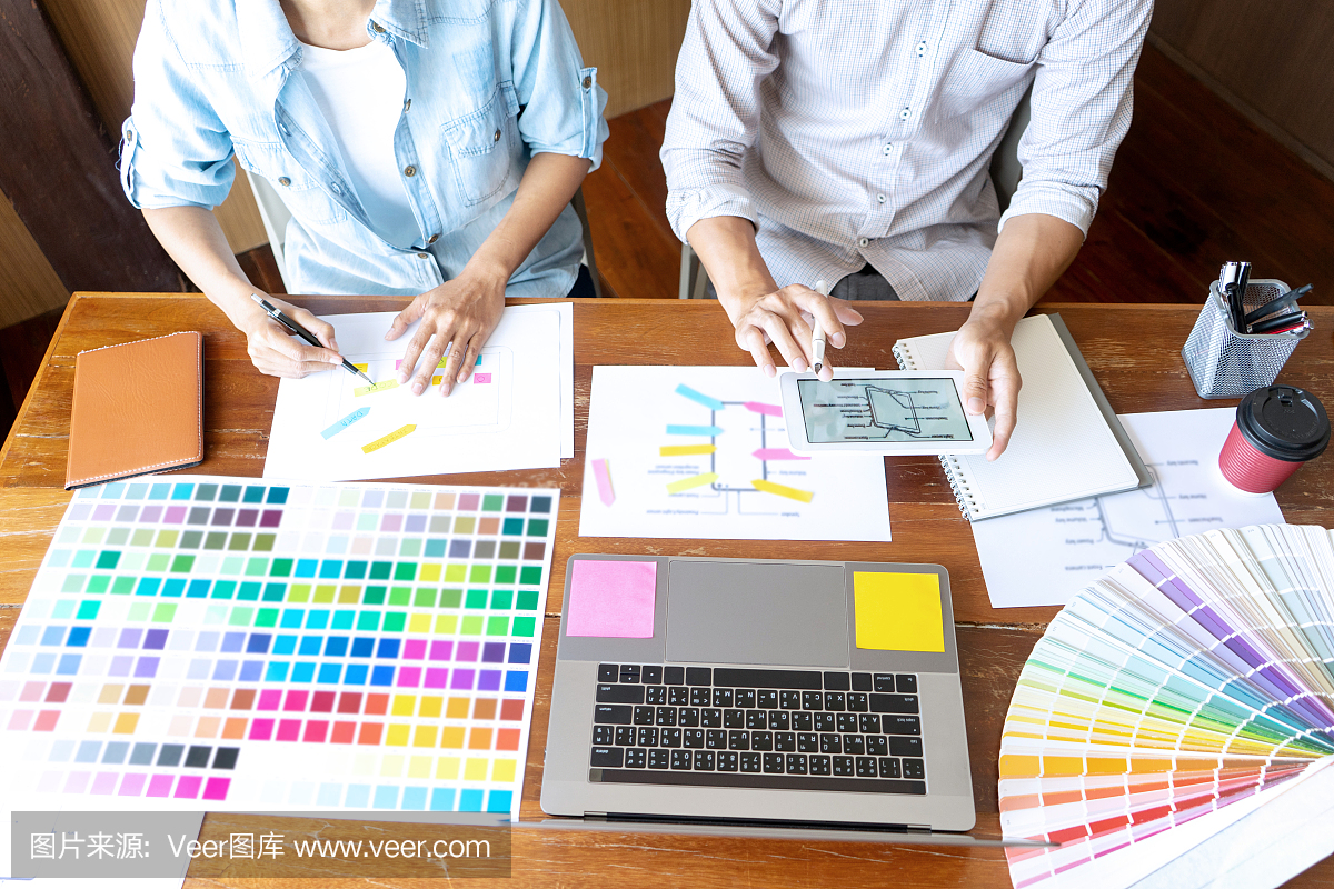 一群年轻的设计师在办公室工作,设计了一款新产品,使用颜色表和电脑笔记本电脑为新的智能手机设计概念